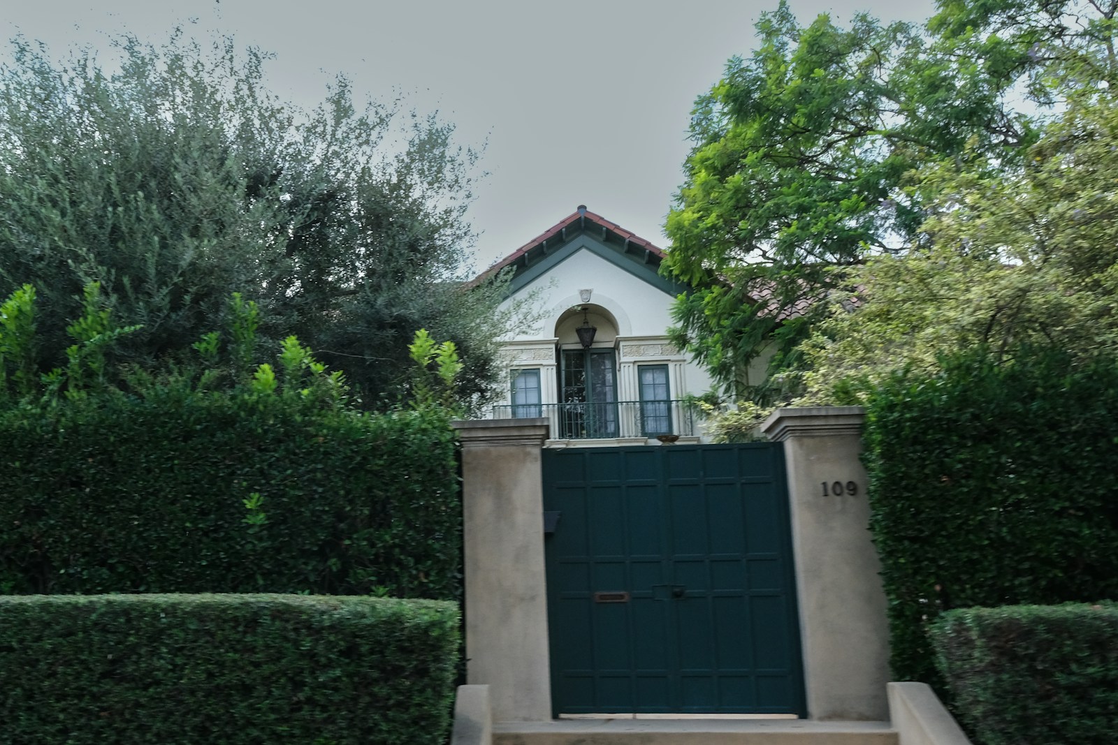 A white house with green gate surrounded by trees.
