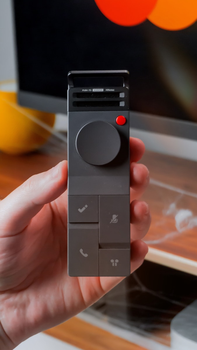 Hand holding a modern gray remote control with buttons.